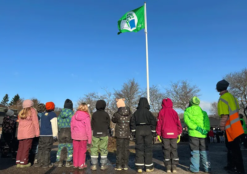 En grön flagga hissas framför en grupp skolbarn.