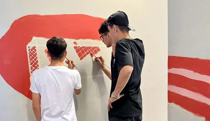 Tre elever står med penslar och målar ett fotbollsmål på en vägg
