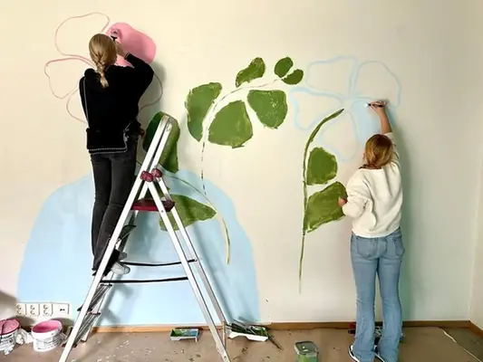 Två elever står med ryggen mot kameran och målar stora blommor på en vägg